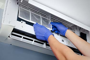Professional air conditioner technician removes filter from indoor HVAC unit to clean for optimum performance
