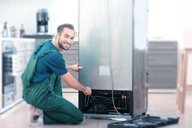 Appliance technician smiling and repairing fridge
