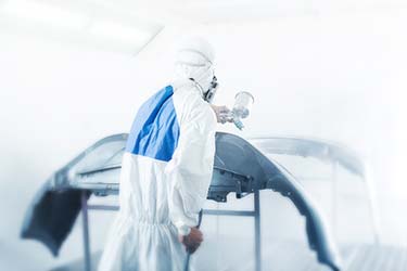 Auto body repair specialist in protective gear, spray painting a car part