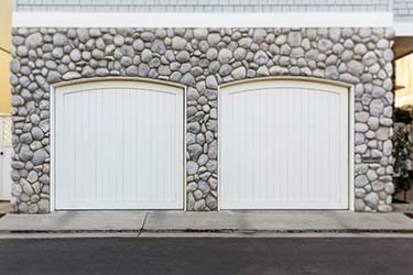Stylish white painted curved wood garage doors fitted into interesting stone building facade