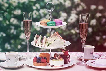 Close up of high tea table spread with champagne, tea, cakes, macarons, and sandwiches