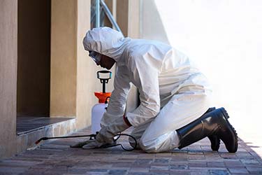 Pest extermination technician in hazmat suit applying pest control treatments to property