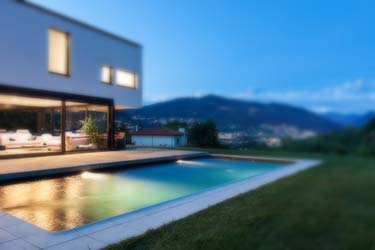 Modern minimalist two-storey home with pool, lit up at night, overlooking valley of homes