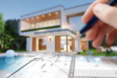 Close up of photograph of stylish home with pool construction plans superimposed over the top, with pencil poised in hand upper right