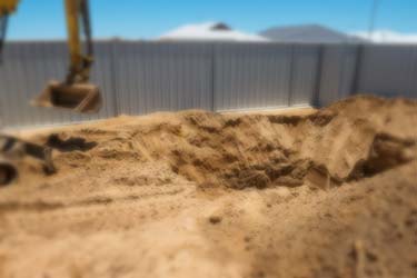 Excavator moving earth from pool construction site, mounds of dirt