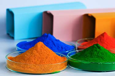 Sample dishes of powder coating pigment colors, with powder coated metal in background