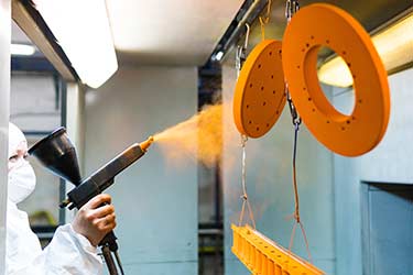 Powder coating technician in protective gear in the process of powder coating metal parts