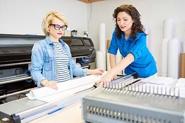 Printing company worker cutting printing supplies with customer in large format print shop