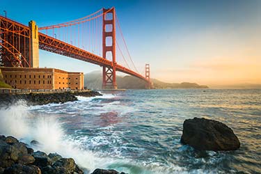 Must-see tourist hotspot, San Francisco Golden Gate Bridge, from the shore below with waves crashing at golden hour