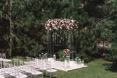 Romantic floral wedding arch and modern clear acrylic seating for outdoor forest wedding