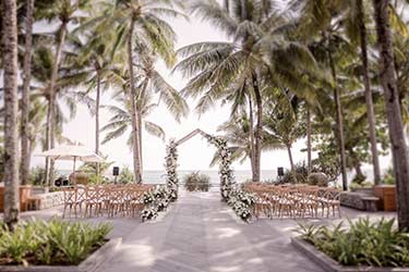 Tropical beach wedding set up with white floral wedding arch and classic wooden chairs