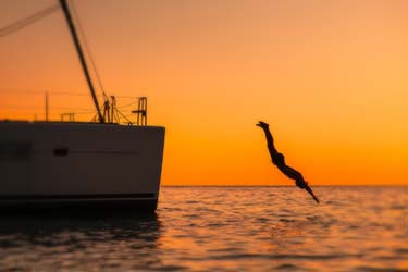 Silhouette of person diving off luxury yacht into ocean at sunset