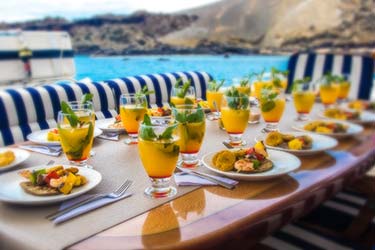 Fresh breakfast setting with tropical fruit juice drinks at table on deck of luxury yacht overlooking tropical coast